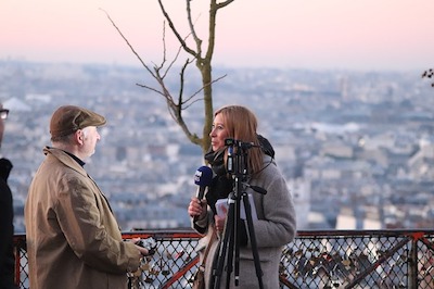 microphone and interviews a man. A city in the background