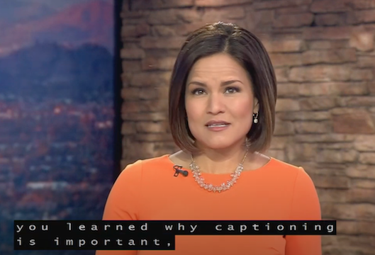 TV studio. Image of a woman news anchor. She has brown hair and eyes and wears an orange top. Superimposed over her chest, a caption reads: "You learned why captioning is important."