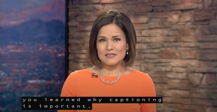 TV studio. Image of a woman news anchor. She has brown hair and eyes and wears an orange top. Superimposed over her chest, a caption reads: You learned why captioning is important