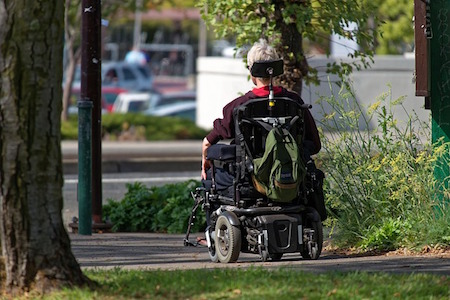 Person in a wheelchair on a paved path facing a road