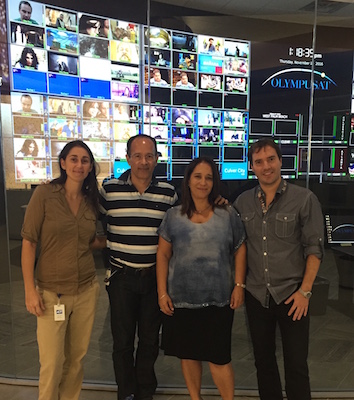 2 men and 2 woman stand next to each other and smile. Behind them a big screen made of 64 TV screens, each TV shows a different image