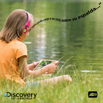 Girl with headphones seated on the grass listens to a video on a tablet. The phrase 
