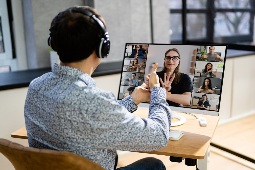 Person using sign language during a video call with multiple participants displayed on a computer screen.