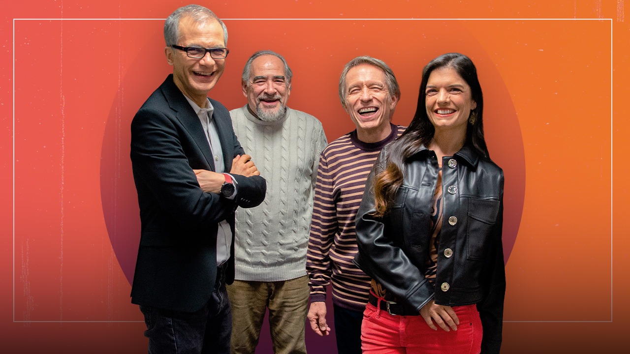 Orange background. Three men with gray hair and a woman, the show "La Dichosa Palabra" hosts, stand smiling.