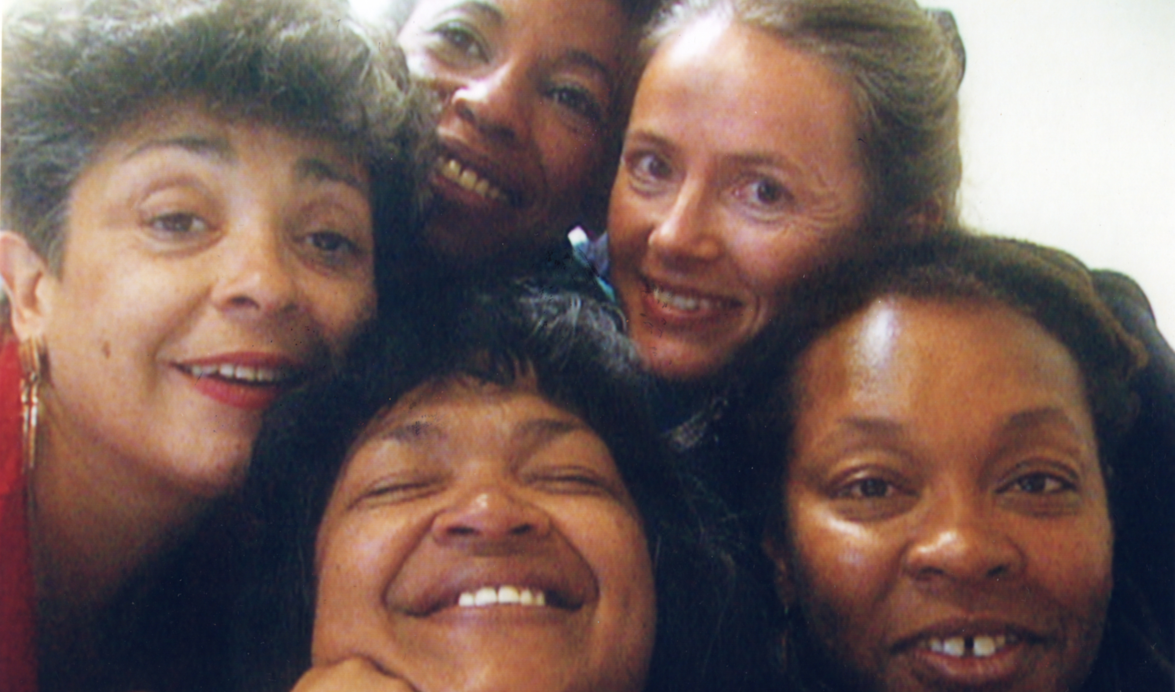 Five women are huddled together, smiling warmly at the camera, suggesting a close and joyful moment.