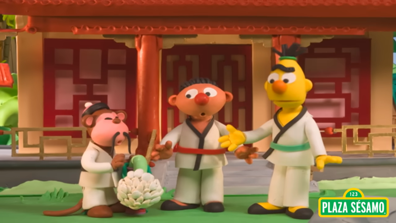 Beto and Enrique stand next to a monkey who is holding a flower in its hand. All three are dressed in Japanese karate suits.