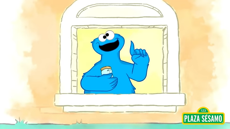 Cartoon. Cookie Monster stands behind a window, he holds a jar in one hand and points with the other as if having an idea