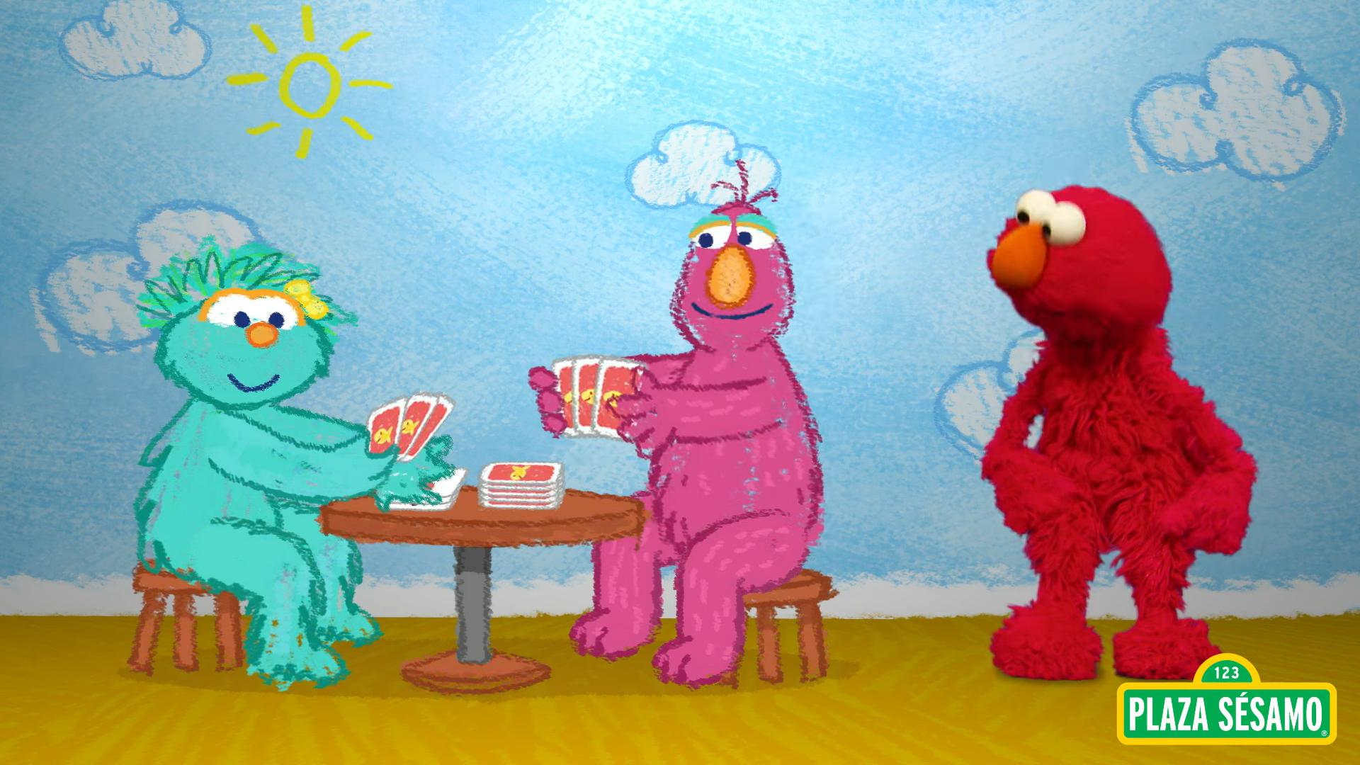 Elmo stands looking to the side at two of his friends sitting at a table playing cards.