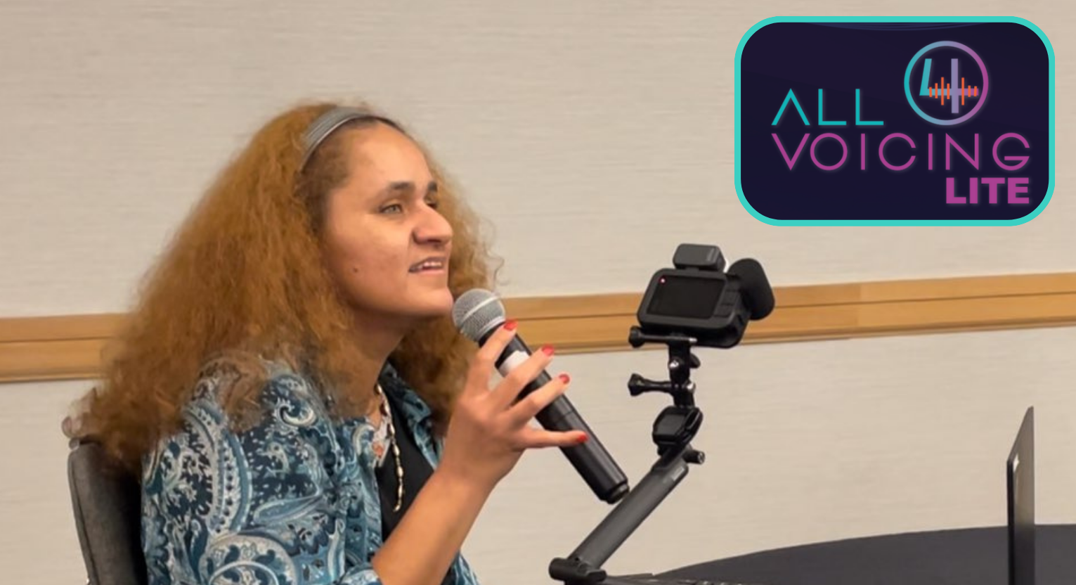 Lucy Arguijo, seated in front of a laptop, holds a microphone and speaks. All4Voicing Lite logo appears on the top right.